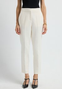 White tailored women's trousers with pleats, slim fit, and a smooth texture, paired with black patent leather heels.