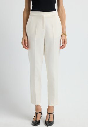 White tailored women's trousers with pleats, slim fit, and a smooth texture, paired with black patent leather heels.