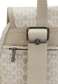 Sac à dos beige avec un motif géométrique, doté d'une sangle texturée et de ferrures argentées. Poche zippée latérale pour plus de fonctionnalité.