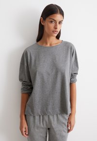 Maglietta grigia a maniche lunghe realizzata in tessuto morbido ed elastico, con una vestibilità comoda e scollo rotondo. Presenta maniche arrotolate e una texture liscia.