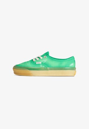 Green canvas sneakers feature a low profile, round toe, white laces, and a translucent gum rubber sole with beige accents.