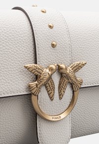 Borsa bianca in pelle con finitura testurizzata, dotata di una chiusura circolare in tono oro con due uccellini innamorati e borchie dorate sulla tracolla.