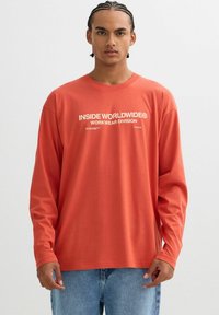 Camisa de manga larga de color óxido, hecha de algodón, con texto impreso en blanco que dice "DIVISIÓN MUNDIAL DE ROPA DE TRABAJO" en el frente.