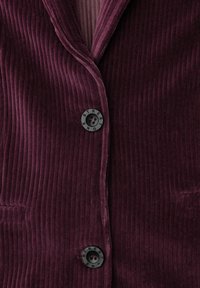 Bordeaux kordfløjl blazer med vertikal ribbet tekstur, spidse lapeller og sorte knapper med ordet "STREET" præget på dem.