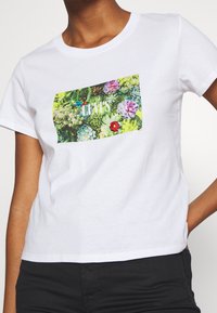 Bílý tričko s krátkým rukávem se čtvercovým grafickým potiskem barevných sukulentů a květin s nápisem "LEVI'S" zabudovaným do designu.