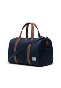 Sac de sport en toile bleu marine avec poignées en cuir marron, bandoulière réglable, fermeture zippée et poche avant. Étiquette Herschel sur le côté.