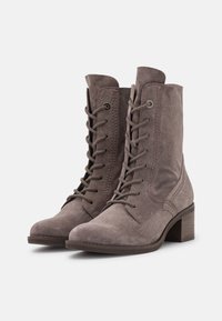 Et par taupe suede lace-up ankelstøvler med stablede blokhæle og afrundede tæer, vist på hvid baggrund.