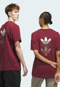 Camiseta de algodón color burdeos con un gran logotipo reflectante de Adidas en la parte posterior, manga corta y un clásico cuello redondo.