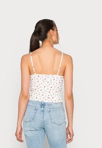 Top de alças finas, branco com padrão de pequenas flores vermelhas; combinado com jeans de cintura alta, azul claro.
