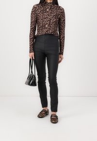 Langarmoberteil mit Leopardenmuster kombiniert mit hoch geschnittenen schwarzen Hosen. Akzentuiert mit einer schwarzen Handtasche und Schuhen im Leopardenmuster.