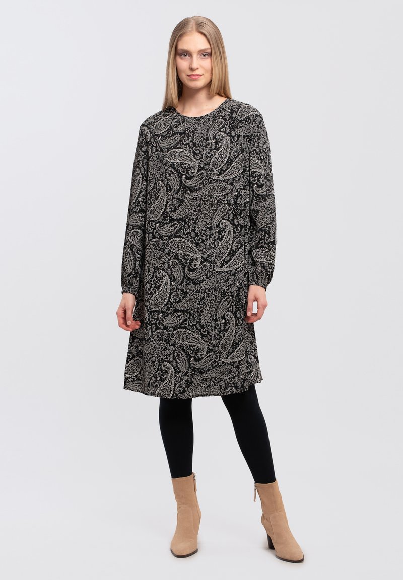 Sort og hvid paisley-mønstret kjole med lange ærmer og rund hals, parret med sorte leggings og beige ankelstøvler.