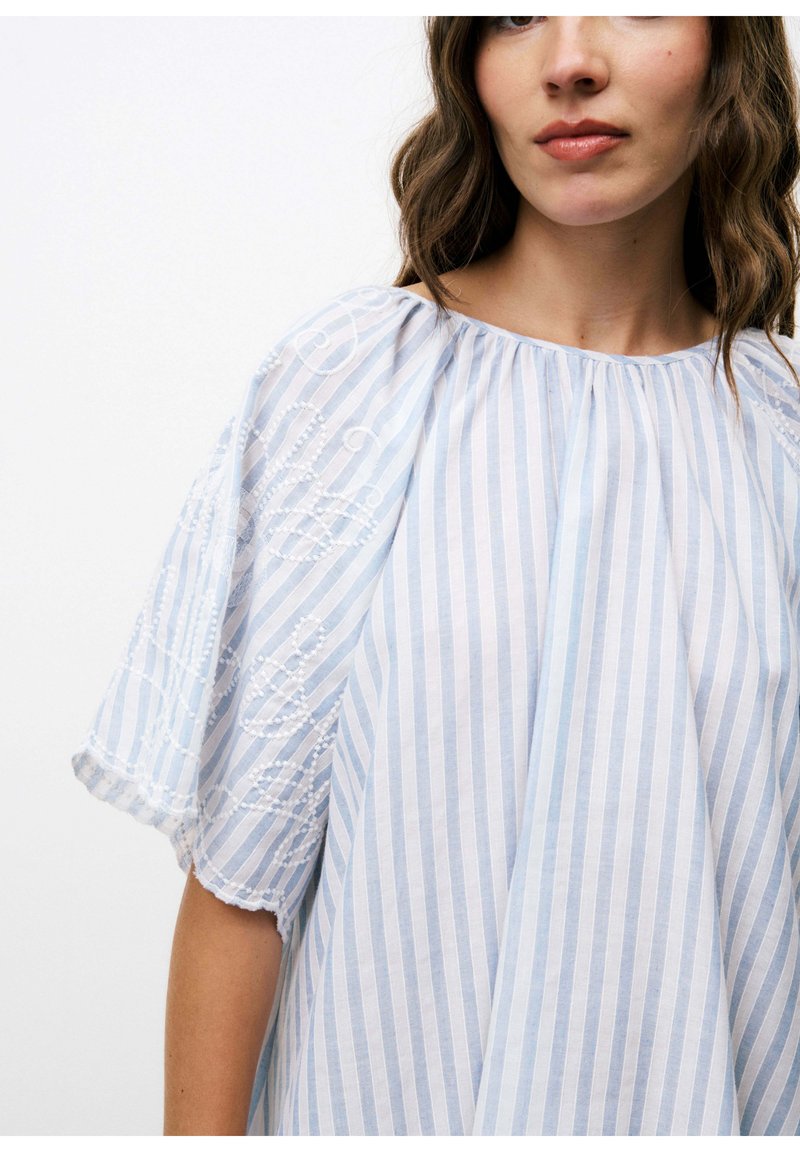 Lichtblauwe en witte gestreepte blouse met korte, geborduurde mouwen. Heeft een losse pasvorm en een ronde halslijn. Gemaakt van een lichte stof.