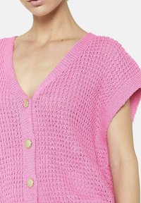 Rozā adīta kardigāna jaciņa ar dziļu V veida kakla izgriezumu, īsām piedurknēm un zeltīta toņa pogu akcentiem. Tekstūrēta auduma pinums piešķir vizuālu interesi.