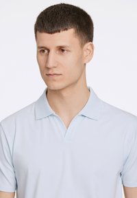 Polo de color azul claro hecho de tela suave. Presenta un cuello clásico y una tapeta de tres botones. Diseño simple y limpio sin estampados.