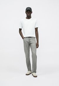 Balta kokvilnas t-krekls, gaiši pelēki džinsi, pelēks beisbola cepures, un bēšas sporta apavi ar brūniem zoliņām. Vienkāršs dizains, brīvs piegriezums, minimālas detaļas.