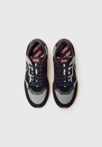 Tênis em camurça azul-marinho, bordô e cinza com detalhes texturizados. Apresenta atacadores com padrão, colarinho almofadado e sola de borracha com detalhe do logotipo.