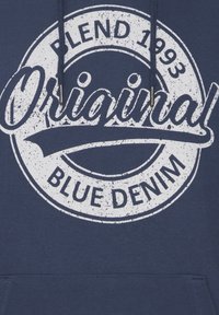 Sötétkék kapucnis pulóver, amelyen egy nagy, megviselt fehér körgrafika látható, rajta az "Original" és "Blue Denim" feliratokkal, valamint a "Blend 1993" felirattal a tetején.