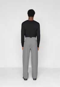 Sive hlače z udobnim krojem, ki imajo gladko teksturo in dve zadnji žep, v kombinaciji z dolgim črnim majico.