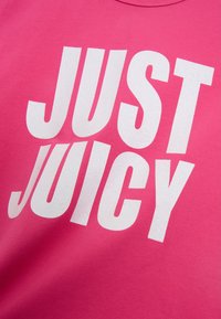 Růžové tričko s velkým bílým třpytivým nápisem "JUST JUICY." Měkká látka s klasickým designem kulatého výstřihu.
