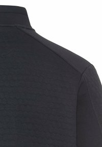 Close-up van een donker polo shirt met een hexagonaal textuurpatroon op de stof, waarbij een deel van de kraag en schouder wordt getoond.