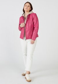 Rosa läderjacka med huva, dragkedja fram och två sidfickor. Bärs över en grå huvtröja och matchas med vita byxor och sneakers.