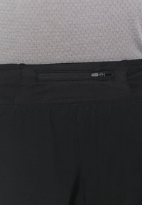 Pantalones deportivos negros de tela suave, con un bolsillo trasero con cremallera segura y un diseño de cinturilla elástica.
