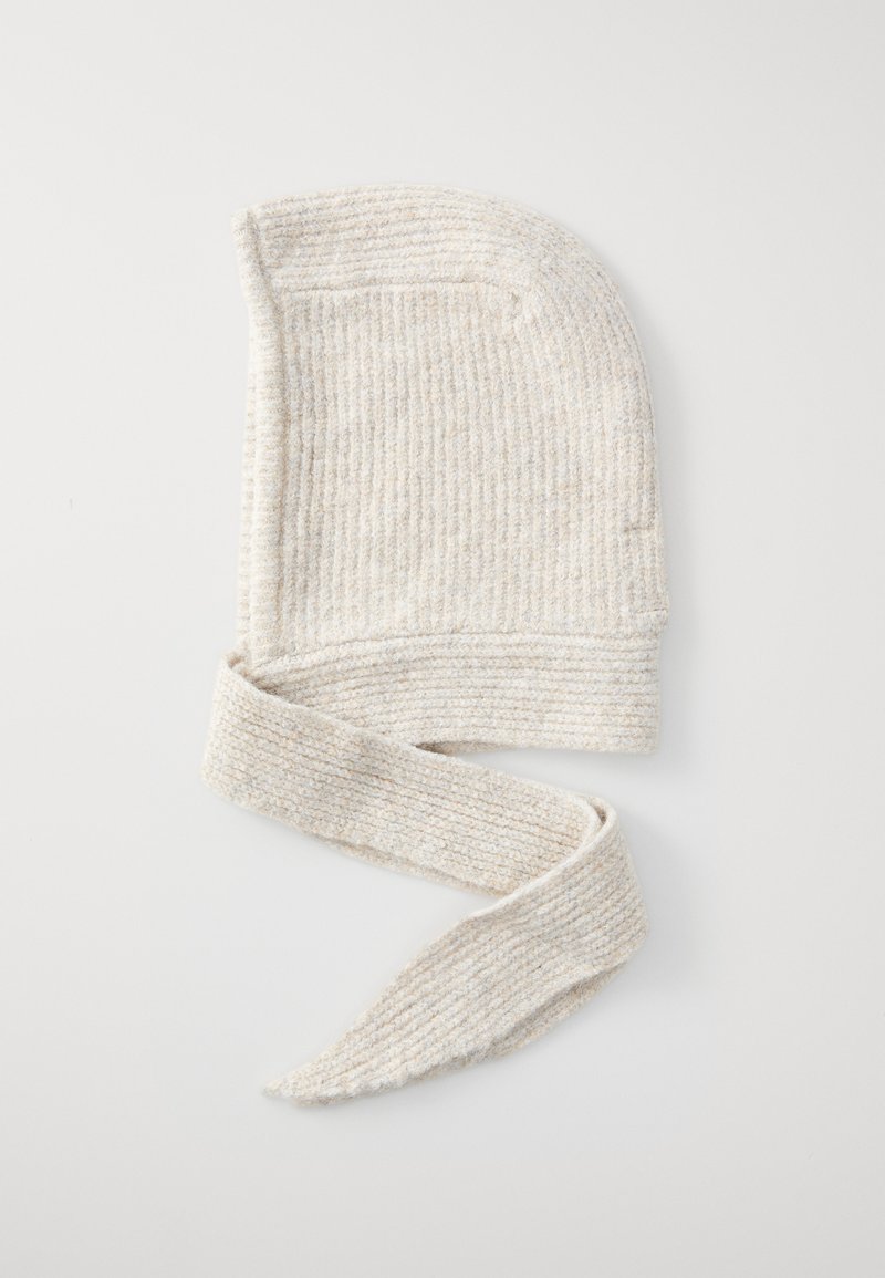 Strikket beige lue med bundet, forlengede sider. Har en ribbestruktur og et mykt, fleksibelt materiale. Ideell for varme og komfort.