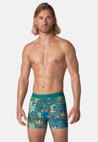 Vīriešu bokseršortiem ar zaļu tropisku rakstu, kurā attēloti putni un augi. Mīksta, elastīga auduma un plata, tumši zaļa josta.