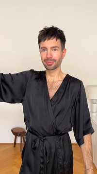 Robe de cetim preto com decote em V profundo, mangas largas e cintura atada. Textura suave, apresentando um design simples e elegante.