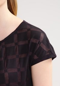 Černý top s krátkým rukávem se síťovan ým kostkovaným vzorem. Hladká textura s výstřihem ve tvaru lodě a ohrnutými rukávy.