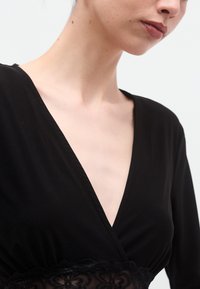 Top negru petrecut, cu decolteu adânc în formă de V, dintr-un material moale și cu dantelă delicată la talie, creând o siluetă structurată.