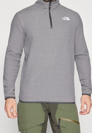 Sudadera gris de forro polar con cremallera hasta el cuarto delantera y cuello alto. Presenta un pequeño logo blanco en el pecho izquierdo y ribetes negros contrastantes en el dobladillo y los puños.