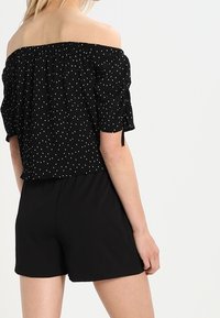 Black off-the-shoulder top with white polka dots, elastic neckline, and short puff sleeves; paired with black shorts, smooth fabric.