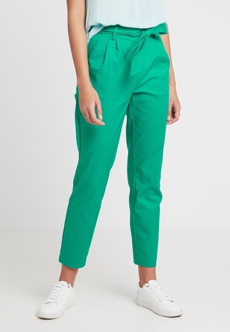 Pantalones verdes ajustados con una cintura alta, presillas para cinturón y bolsillos laterales. Tela suave, diseño de pierna tapered, combinados con zapatillas blancas.