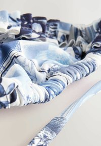 Tessuto blu a motivo con texture arricciata, caratterizzato da volant lungo il bordo. Il design include diverse tonalità di blu e motivi intricati.