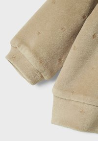 Beige fleecestof met subtiele gouden spikkels aan de mouwen. Dikke structuur met een zachte afwerking en omgeslagen uiteinden voor een aansluitende pasvorm.