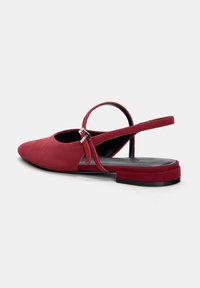 Rote Wildleder-Slingback-Schuhe mit spitzem Fuß, schmalem Knöchelriemen und flacher schwarzer Sohle. Mit metallischem Schnallenakzent.