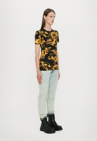 Svart t-skjorte med gul utsmykking, rund hals, korte ermer, kombinert med lyse denimjeans og svarte snørebåndsstøvler.