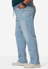 Pantalones de mezclilla azul claro con un corte relajado, que presentan detalles desgastados y una cintura con cordón, combinados con zapatillas ligeras.