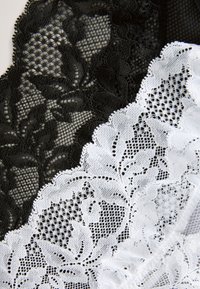 Juodos ir baltos nėriniai audinio gabalėliai, turintys gėlių raštus ir sudėtingus dizainus. Tekstūros yra permatomos su banguotomis kraštinėmis.