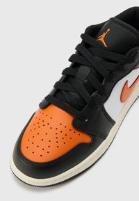 Sneaker in pelle nera e arancione con punta perforata, pannelli bianchi, lacci neri e logo Nike arancione. Suola in gomma, design con punta tonda.