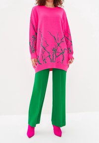 Hett rosa oversized tröja med ett grönt trädliknande mönster, kombinerad med vida gröna byxor och klara rosa stiletthälar.