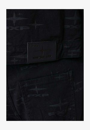 Black canvas pants featuring a tone-on-tone logo pattern and a rectangular brand label stitched at the waistband, with a visible back pocket.