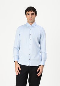 Lichtblauw overhemd met lange mouwen en een spitse kraag, voorzien van bruine knopen en een gladde textuur, gecombineerd met zwarte broek.