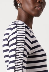 Top a righe navy e bianche con una vestibilità aderente, caratterizzato da dettagli arricciati lungo la cucitura delle maniche e una texture in cotone morbido.