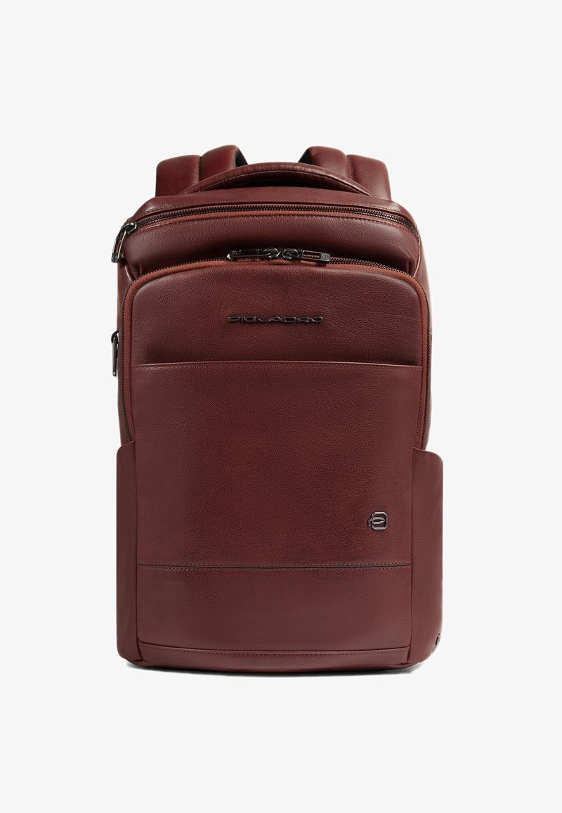 Sac à dos en cuir marron au design structuré, avec une poche avant zippée et une pochette latérale. Texture lisse et logo embossé sur le devant.