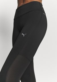 Leggings neri con vita alta, texture liscia e pannelli in rete con un motivo a pois. Un logo Puma riflettente è posizionato sulla coscia.