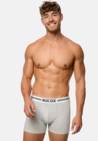 Grijze katoenen boxershorts met een elastische tailleband met zwart-witte strepen, waarop de merknaam "INDICODE" prominent is afgebeeld.
