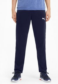 Navy athletic pants made of a smooth fabric, featuring a white Puma logo on the left thigh, with a tapered fit and elastic waistband.