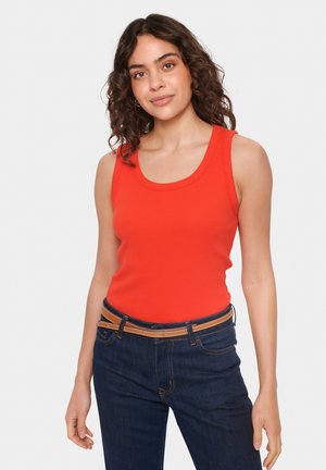 Top corto rosso a costine con scollatura a girocollo, abbinato a jeans blu scuro con una cintura marrone chiaro e dettagli di cucitura.